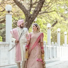 A beautiful portrait of a Sikh couple on their wedding day, standing together in a serene outdoor setting with elegant white pillars.