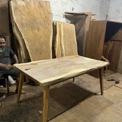 A live-edge table being prepared in the workshop. In the background, you can see the large, raw slabs of wood that I source to create these unique, one-of-a-kind tabletops.
