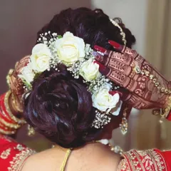 A close up of the bride's hands as she adjusts her floral hair bun. The intricate back hand mehendi looks beautiful against her traditional attire.