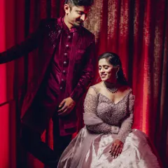 A stylish, posed portrait of the couple at their Sangeet. The rich colors of their outfits and the dramatic red background create a glamorous, high-fashion look.