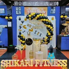 A full view of the gym anniversary celebration setup. The decor includes a balloon arch, themed backdrop, and marquee letters, creating a festive atmosphere right on the gym floor.
