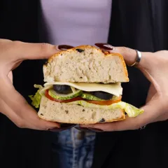 A simple, appealing shot of a sandwich held in two hands, focusing on the fresh layers of vegetables and cheese.