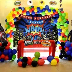 An action-packed superhero birthday party with a comic book "WHAM!" backdrop, character standees of Captain America and Black Panther, and a vibrant balloon arch.
