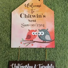 A cute, hut-shaped nameplate for 'Chitwin's Nest,' featuring two owls. The names of the couple hang below on a separate wooden plaque.
