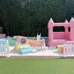 A complete pastel-themed soft play area set up outdoors, featuring a pink bounce castle, a ball pit, and various soft play elements for climbing and exploring.
