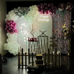 A low-light view of the pink and silver birthday setup, showcasing how the neon sign and shimmer wall create a magical glow. This ambiance is perfect for evening celebrations and adds a sophisticated touch to the party.