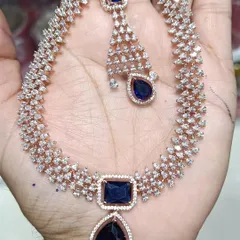 A beautiful American Diamond necklace set with a large sapphire-blue stone. This set comes with matching earrings and a maang tikka, offering a complete, modern look for any party.