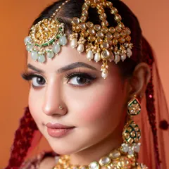 A detailed portrait that captures both the eye makeup and the elaborate hair accessories. The crisp focus allows potential clients to inspect the liner, lashes, and the fine craftsmanship of the kundan and pearl maang tikka and passa.