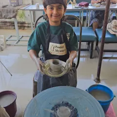Success. Holding up his first wheel-thrown pot, this little artist is all smiles. Every child takes home what they make, a tangible reminder of their creative achievement.