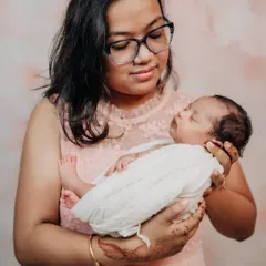 A mother cradling her precious newborn. The soft pink backdrop and simple styling keep the focus entirely on the love and tenderness of the moment.