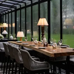 A long, live-edge wooden table provides a communal dining option at FIORI. This element, paired with comfortable high-chairs, adds a rustic yet sophisticated touch that complements the restaurant's nature-inspired theme.