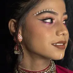A creative airbrush makeup look featuring decorative pearl bindis and sharp, graphic eyeliner. This demonstrates how airbrush techniques can be used for both a flawless base and artistic details.