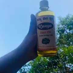 Holding up a bottle of my golden-hued Kanya Hair Oil against the sky. The color comes from the rich blend of over 40 natural herbs infused in coconut oil.