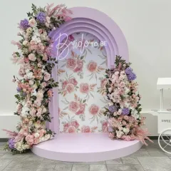 A chic and modern photo booth for a bridal shower or Mehendi. The lilac-colored arch is adorned with pastel flowers and a 'Bride to be' neon sign, creating a perfect spot for pictures.