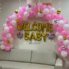 For a simple and sweet welcome, I can create a beautiful balloon arch right above your sofa. This design uses pink and white balloons with gold 'WELCOME BABY' letters, instantly making your living room feel festive.