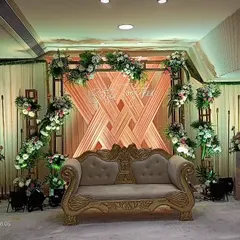 A contemporary stage backdrop for an engagement or reception. This design features a woven pattern of peach-colored fabric on a metal frame, adorned with beautiful floral arrangements.
