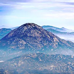 A classic view of Nandi Hills on a misty morning. The fog rolling through the valleys creates a beautiful, layered effect, making the main peak stand out. This is a popular spot for landscape photography near Bangalore.