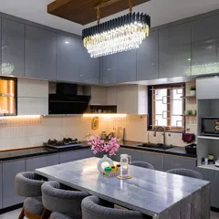 This is a modern kitchen designed for both cooking and conversation. It features sleek grey cabinetry, a stunning chandelier, and a marble-topped island that doubles as a dining space, making it the true heart of the home.