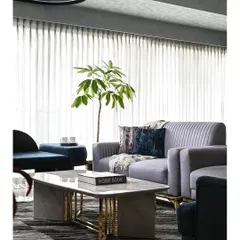 A serene living room where a neutral grey palette is enlivened by deep blue accents. The space is unified by luxurious materials, including a marble coffee table with brass legs and plush, fluted sofas, all set against sheer curtains that bathe the room in soft, natural light.