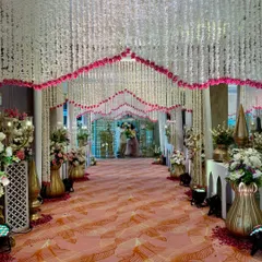 A beautiful walkway for a beautiful beginning. I created this grand entrance with a dense canopy of white and pink floral strings, leading guests down a patterned carpet flanked by traditional brass decor for an elegant wedding reception.