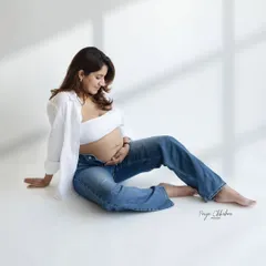 A quiet moment of reflection. This minimalist studio shot, with its clean background and casual styling, puts all the focus on the mother's peaceful connection with her baby bump.