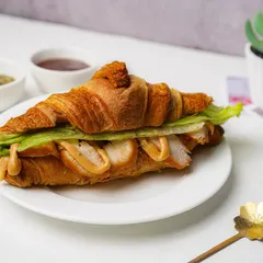 A gourmet croissant sandwich filled with sliced chicken, fresh lettuce, and a creamy sauce, presented on a clean white plate. This shot is styled for a cafe menu, emphasizing the fresh ingredients and flaky pastry.