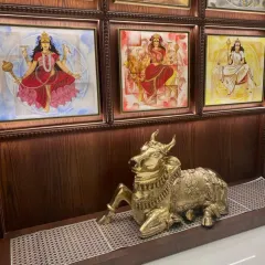 A close-up of a spiritual corner in a home, featuring a gallery wall of goddesses and a brass Nandi statue. This arrangement creates a sacred space for reflection and prayer.