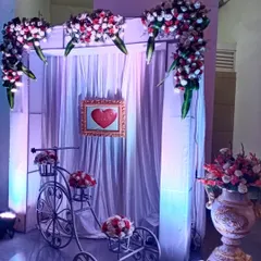 I can create charming photo corners for your guests. This setup includes a decorative white bicycle filled with flowers, set against a simple backdrop of white drapes and soft lighting for a romantic photo spot.