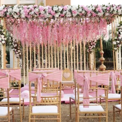 A beautiful pink and gold mandap for a day wedding. The design features hanging pink wisteria, golden pillars, and elegant seating for a classic, romantic ceremony.