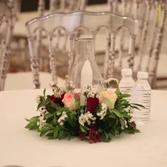 A simple yet beautiful table centerpiece featuring a candle in a glass hurricane lamp, surrounded by a wreath of fresh red and white flowers.