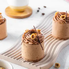 An exquisite hazelnut and chocolate mousse dessert, styled with a minimalist aesthetic. The focus is on the intricate piping work and delicate decorations, showcasing the artistry of the pastry chef on a clean, white background.