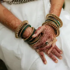 A close-up of the bride's hands, adorned with intricate henna and beautiful green and gold bangles. A perfect shot of traditional bridal details.