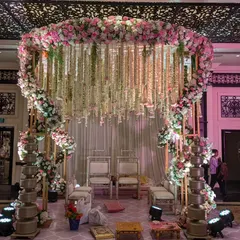 This circular mandap is designed for an intimate yet grand ceremony. A ring of pink and white florals is suspended overhead, with delicate floral strings cascading down, creating a romantic and ethereal space for the vows.