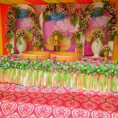 A full view of a Haldi decoration setup, showing the stage with floral arrangements, traditional urlis, and a colorful fabric canopy.