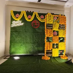 A traditional marigold backdrop for a baby shower, featuring a neon sign and lotus flower cutouts.