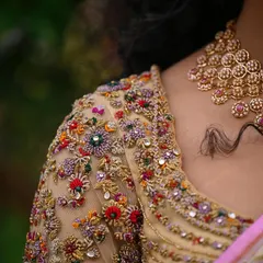 The shoulder and neckline of a custom blouse, adorned with a garden of embroidered flowers and crystals. This detail shot highlights the craftsmanship that goes into creating a wearable piece of art.