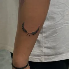 A simple and elegant laurel leaf tattoo on the forearm. This minimalist design is a classic symbol of victory and honor, created with delicate, clean lines.