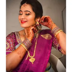 Putting on the final touches. Her makeup was designed to highlight her features, with defined brows, winged eyeliner, and a bright lip color that complements her purple and grey saree.
