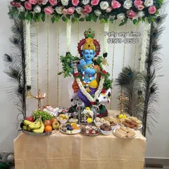 A beautiful setup for Krishna Janmashtami, including a floral canopy with peacock feathers and a table for offerings.