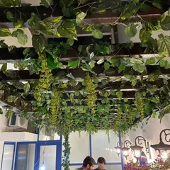This wooden pergola is densely covered with artificial money plant and wisteria vines, creating a lush green canopy over an outdoor seating area.