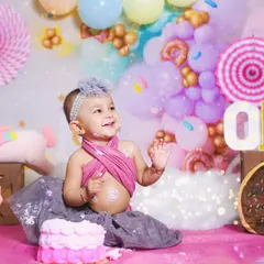 A sweet celebration in a custom Candyland setup. This little girl is enjoying her first birthday cake surrounded by pastel balloons, donuts, and a unicorn friend.