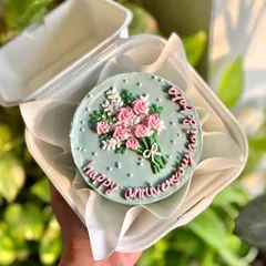 The floral anniversary bento cake, held in hand to show its cute, personal size. Perfect for a sweet, intimate celebration.