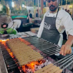 My chef carefully tends to long skewers of seekh kebabs on the grill. The open flames create a beautiful char, ensuring each kebab is cooked through and packed with flavor.