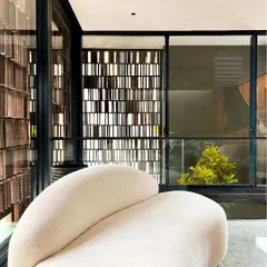 This living space is designed to frame a view of the landscaped courtyard. A curved sofa is oriented towards the outdoors, where a concrete jali screen provides privacy and passive cooling, reinterpreting vernacular strategies in a modern context.