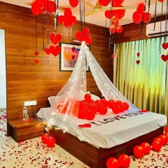 I create deeply romantic moments with setups like this. The room is filled with red balloons, a floor scattered with rose petals, and a bed featuring "I LOVE YOU" spelled out, all under a dreamy, lit canopy.
