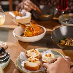 Sharing is at the heart of the Comorin experience. A hand reaches for our signature Cheeni Malai Toast, surrounded by other small plates ready to be passed around.