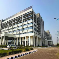 A perspective view of the Indraprastha Medical Institute, showing the main entrance and the building's impressive scale. The design incorporates clean lines and extensive landscaping for a modern, professional feel.