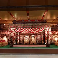 This unique wedding stage is designed to resemble a traditional temple sanctum, complete with carved deity figures. The red and white floral decorations add to the sacred and authentic atmosphere of the ceremony.