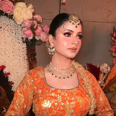 A close-up of the makeup and hairstyle for the orange lehenga look. The hair is styled in a chic, traditional bun with delicate baby hairs.