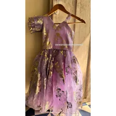 A magical party dress for a little princess. This lavender creation features a gold foil print on a sheer overlay, an asymmetrical neckline, and a single ruffled sleeve for a touch of whimsy.